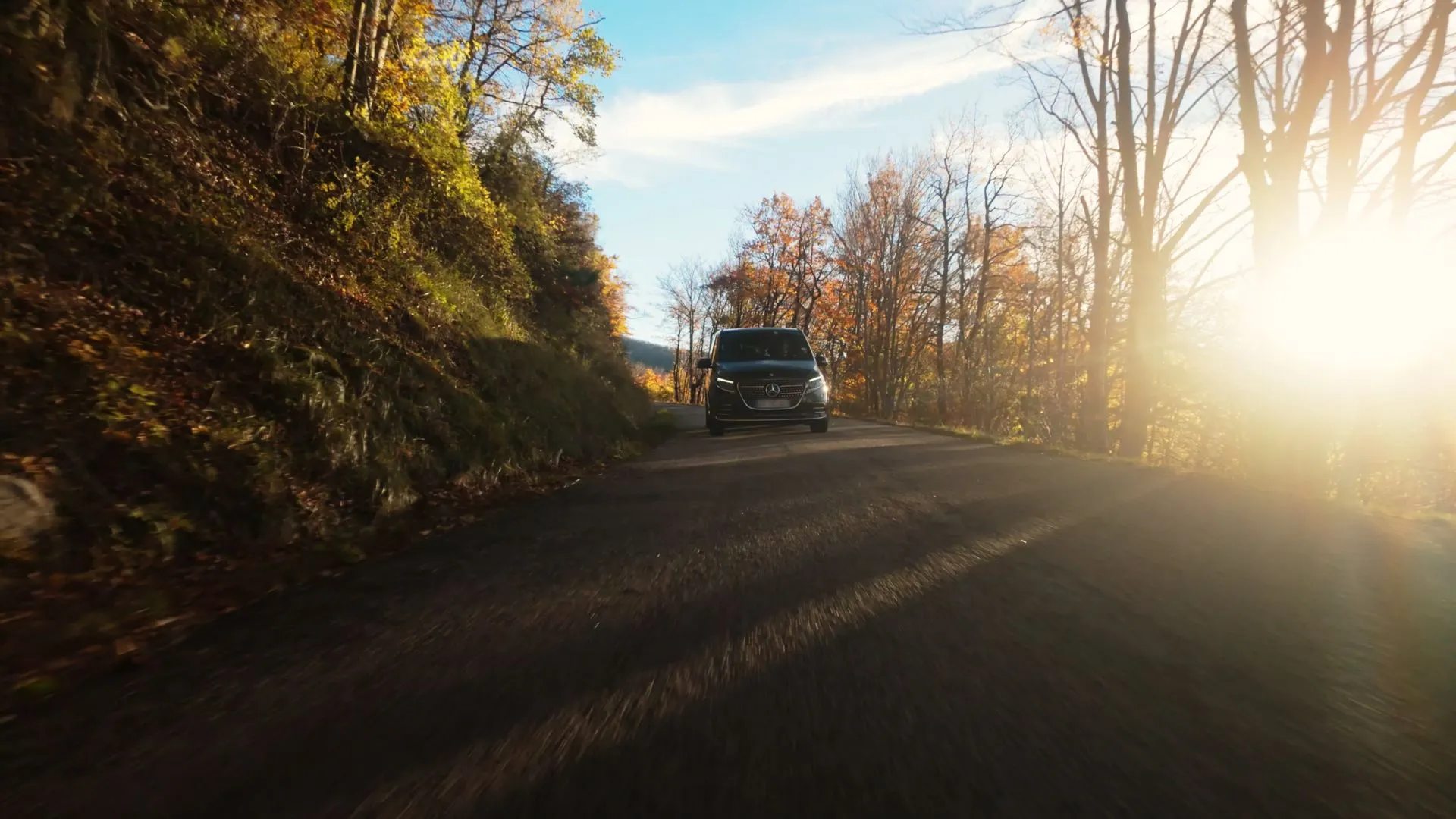 Van noir sur une route de campagne en automne, à contre-jour