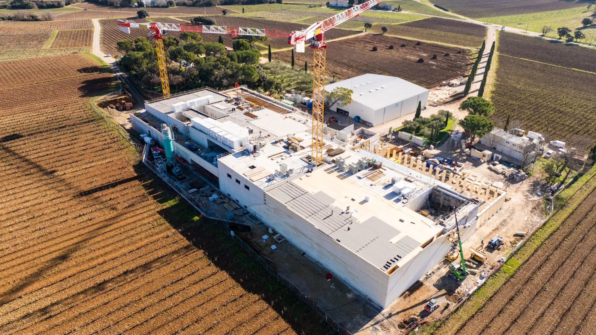 Vue aérienne d'un bâtiment en construction et de sa grue, entouré de champs