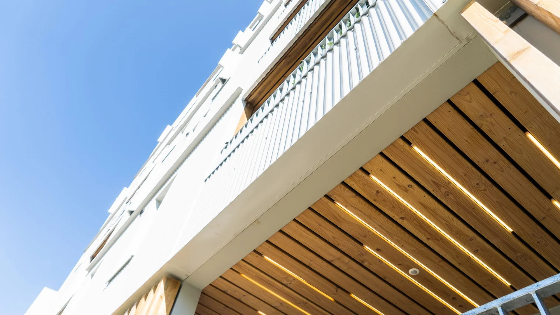 Contre-plongée sur le débord de toiture d'un bâtiment bois et blanc