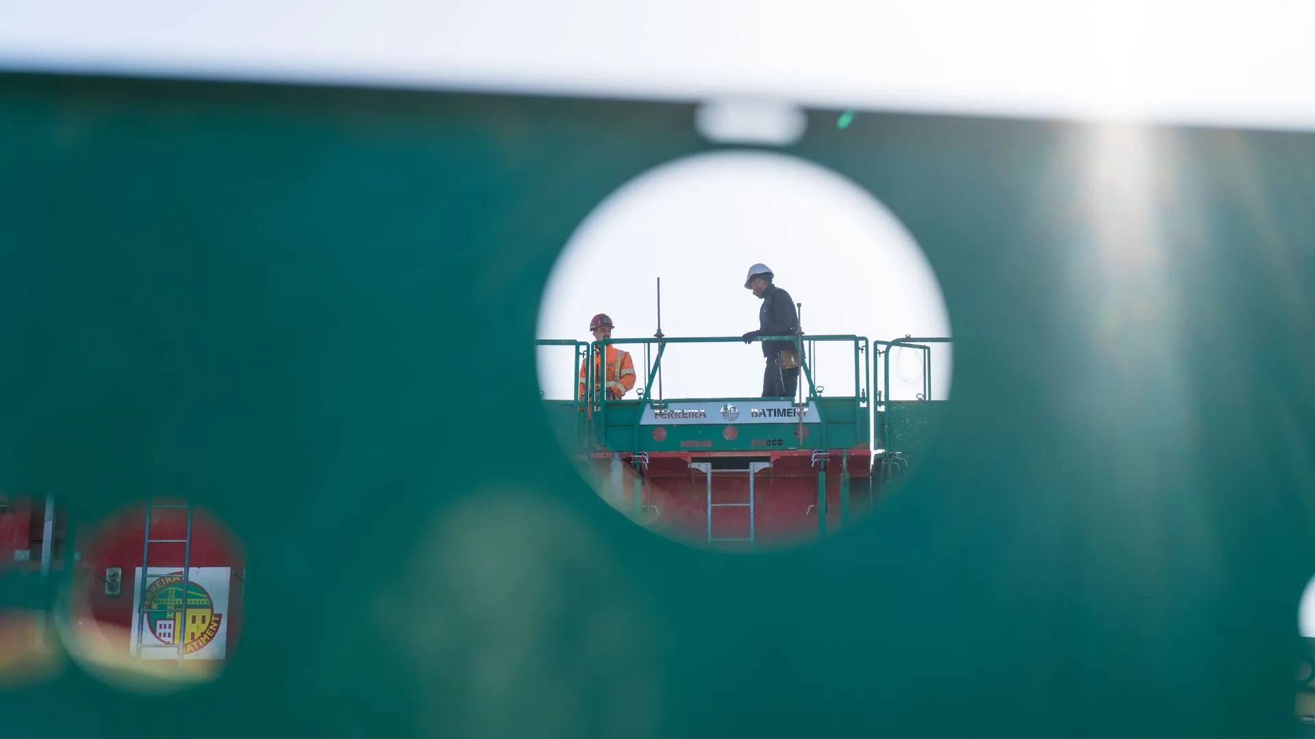 Deux ouvriers sur une nacelle, aperçus à travers une ouverture vitrée