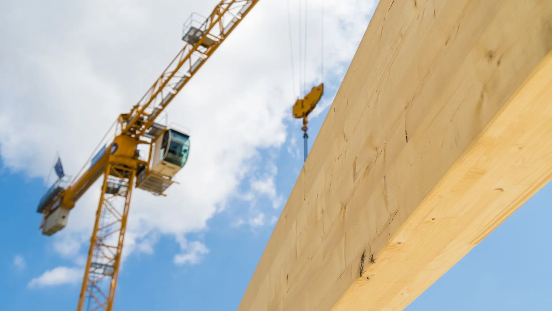 Grue jaune soulevant un élément le long d'une façade béton