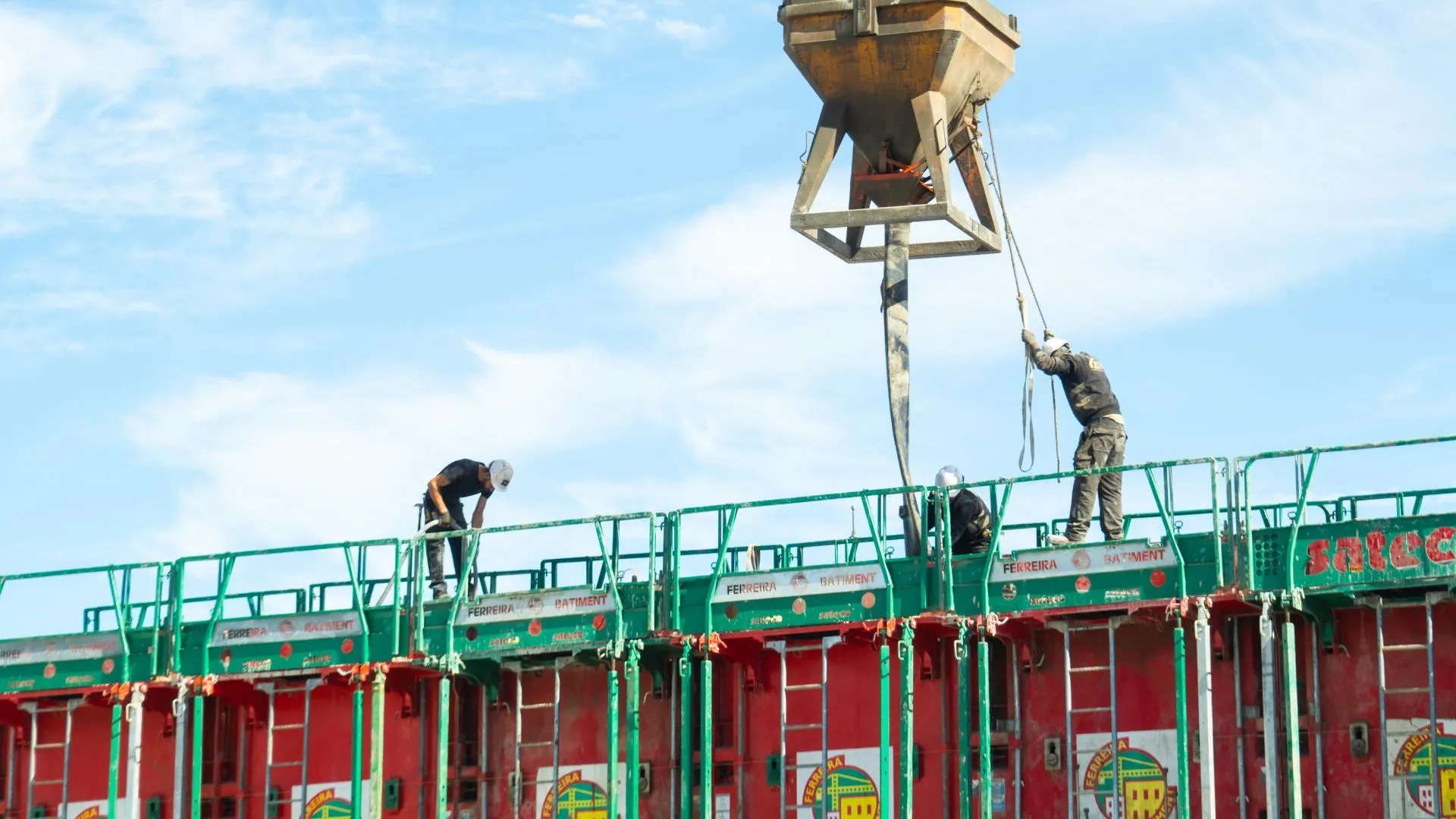 Benne à béton suspendue à la grue au-dessus des banches, ouvriers au travail