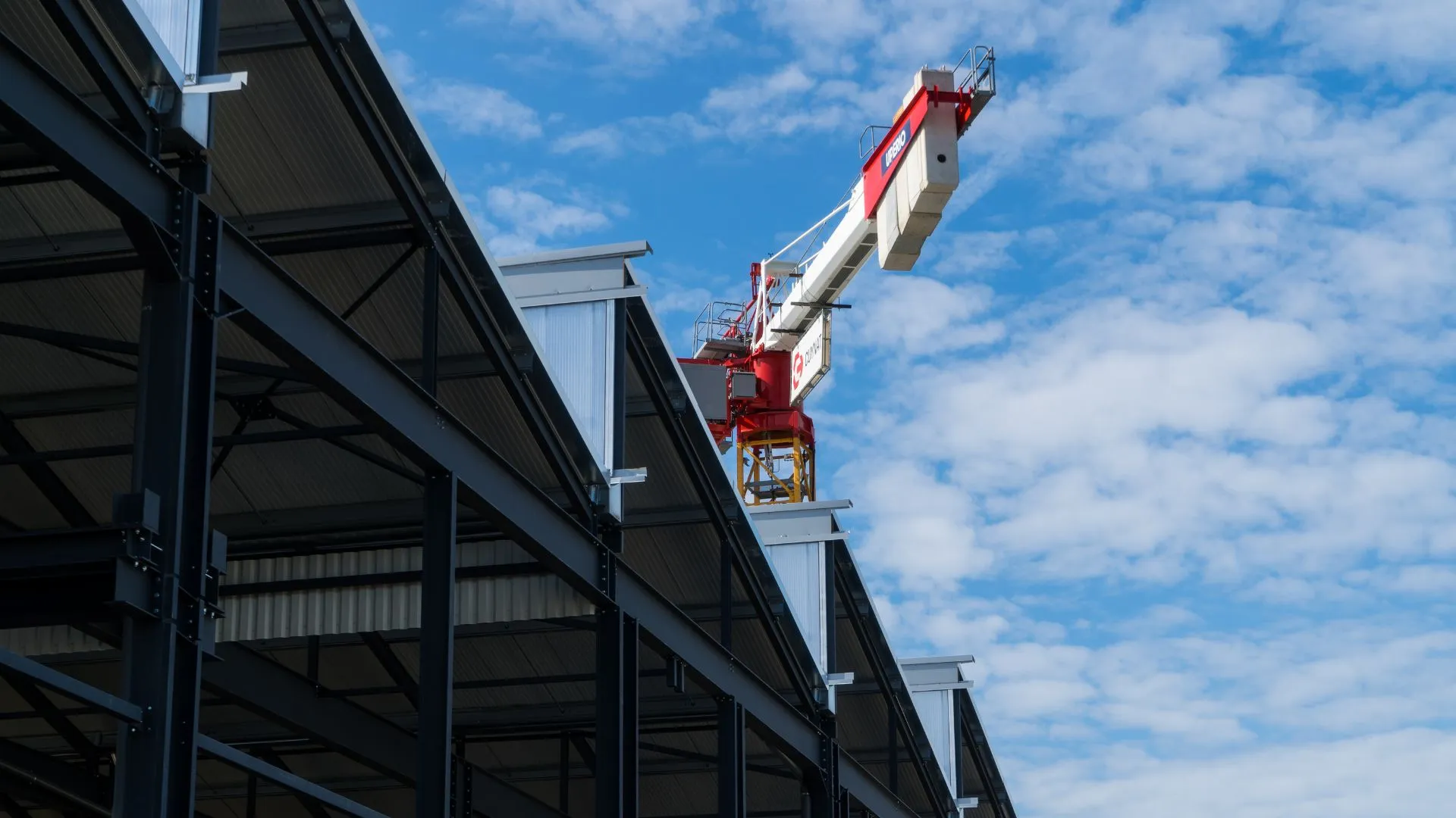 Charpente métallique d'un bâtiment en construction et grue rouge sous un ciel bleu