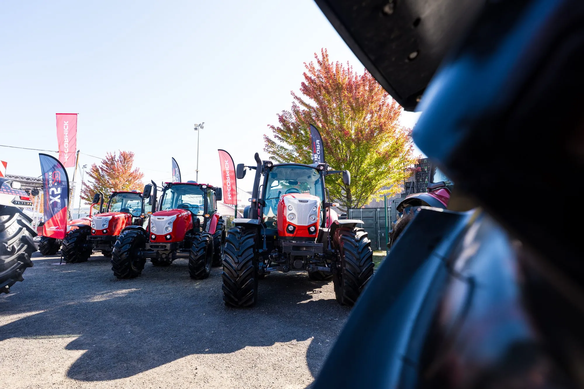 Alignement de tracteurs McCormick exposés sur le stand, ciel bleu et feuillage d'automne
