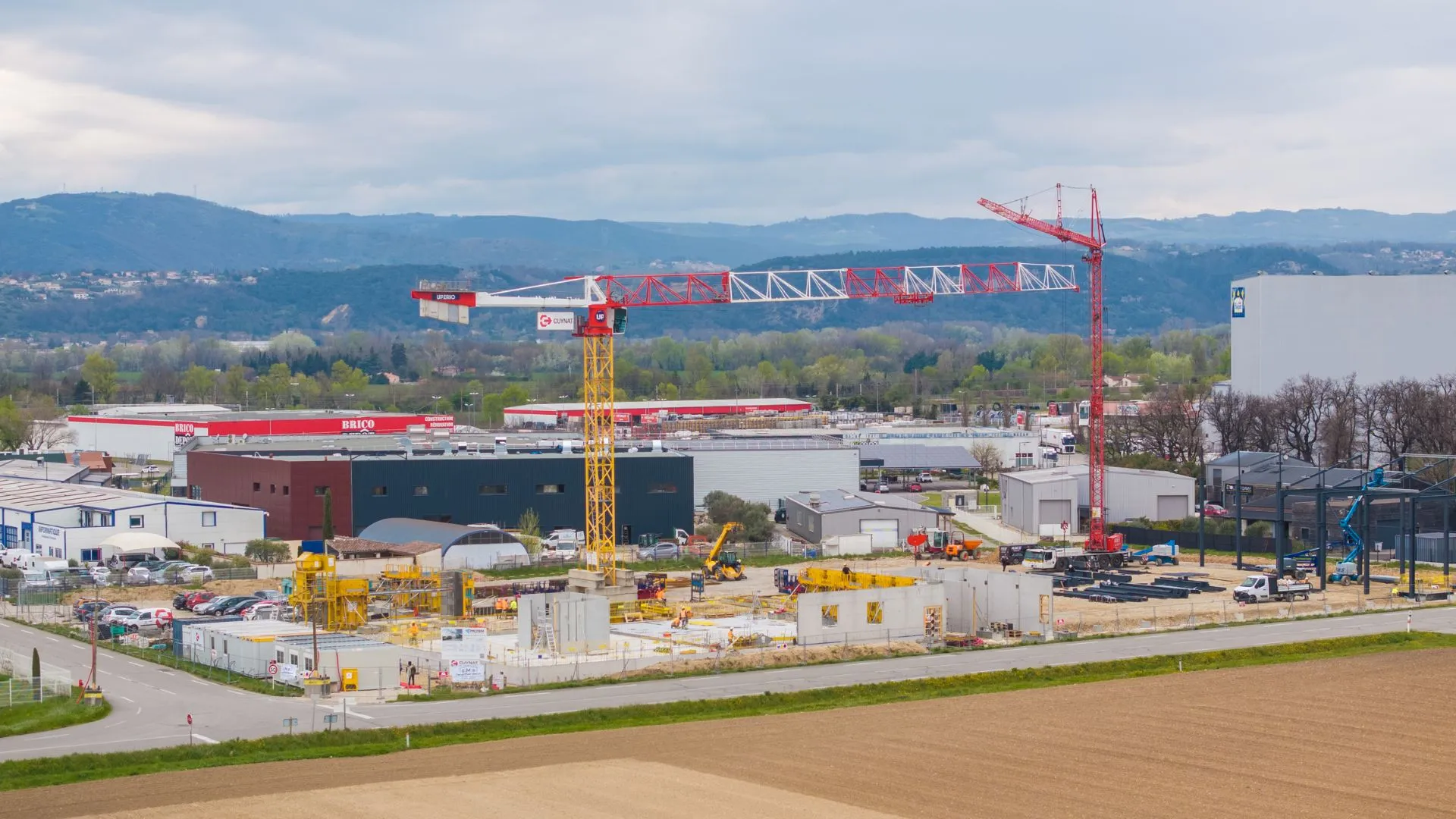 Vue aérienne du chantier en phase de fondations avec grue à tour, zone d'activités