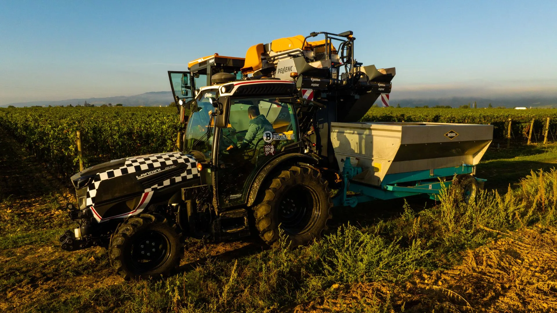 Tracteur et machine à vendanger Pellenc dans les vignes à l'heure dorée