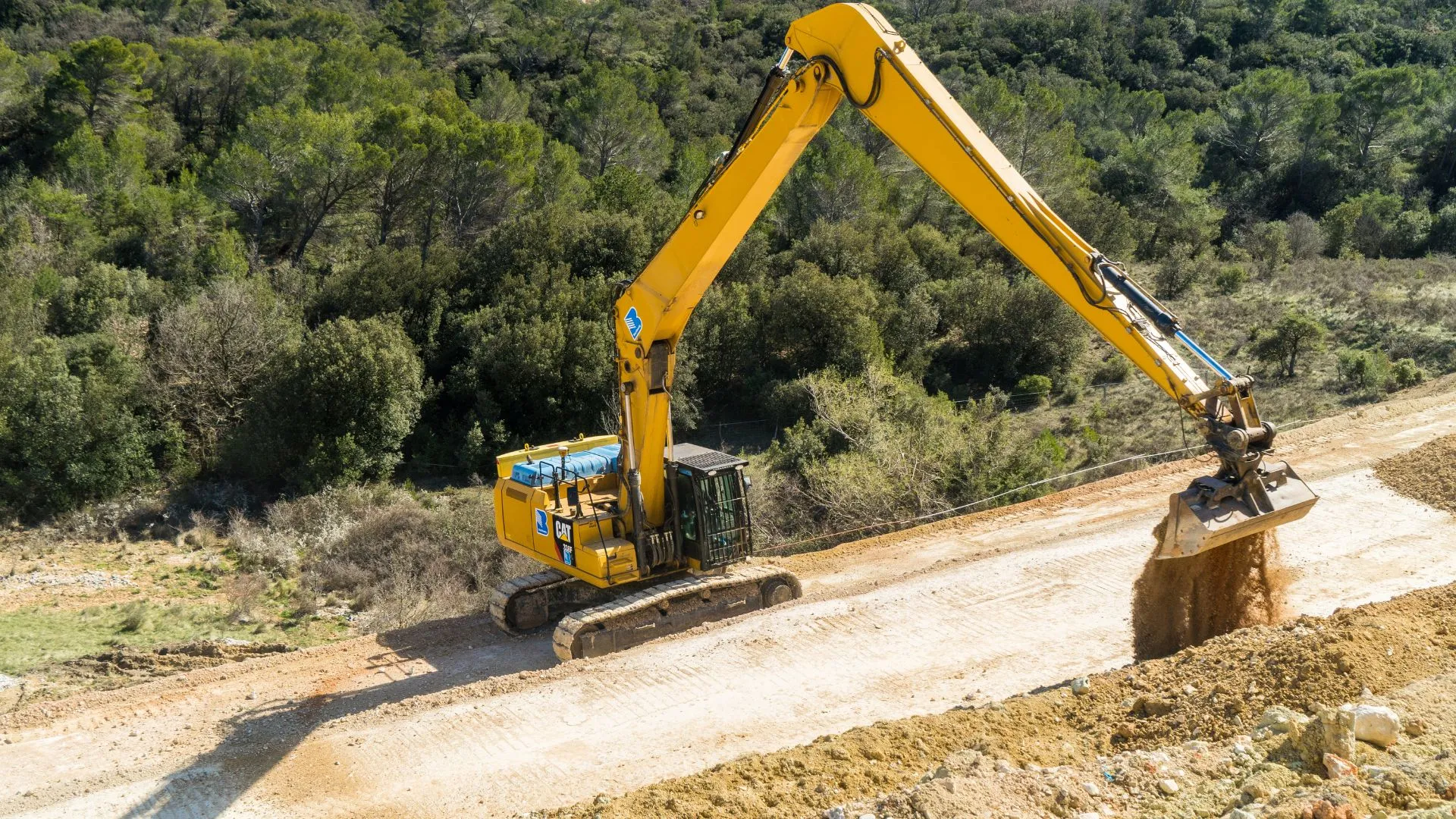 Pelle mécanique jaune façonnant la plateforme routière en lisière de forêt