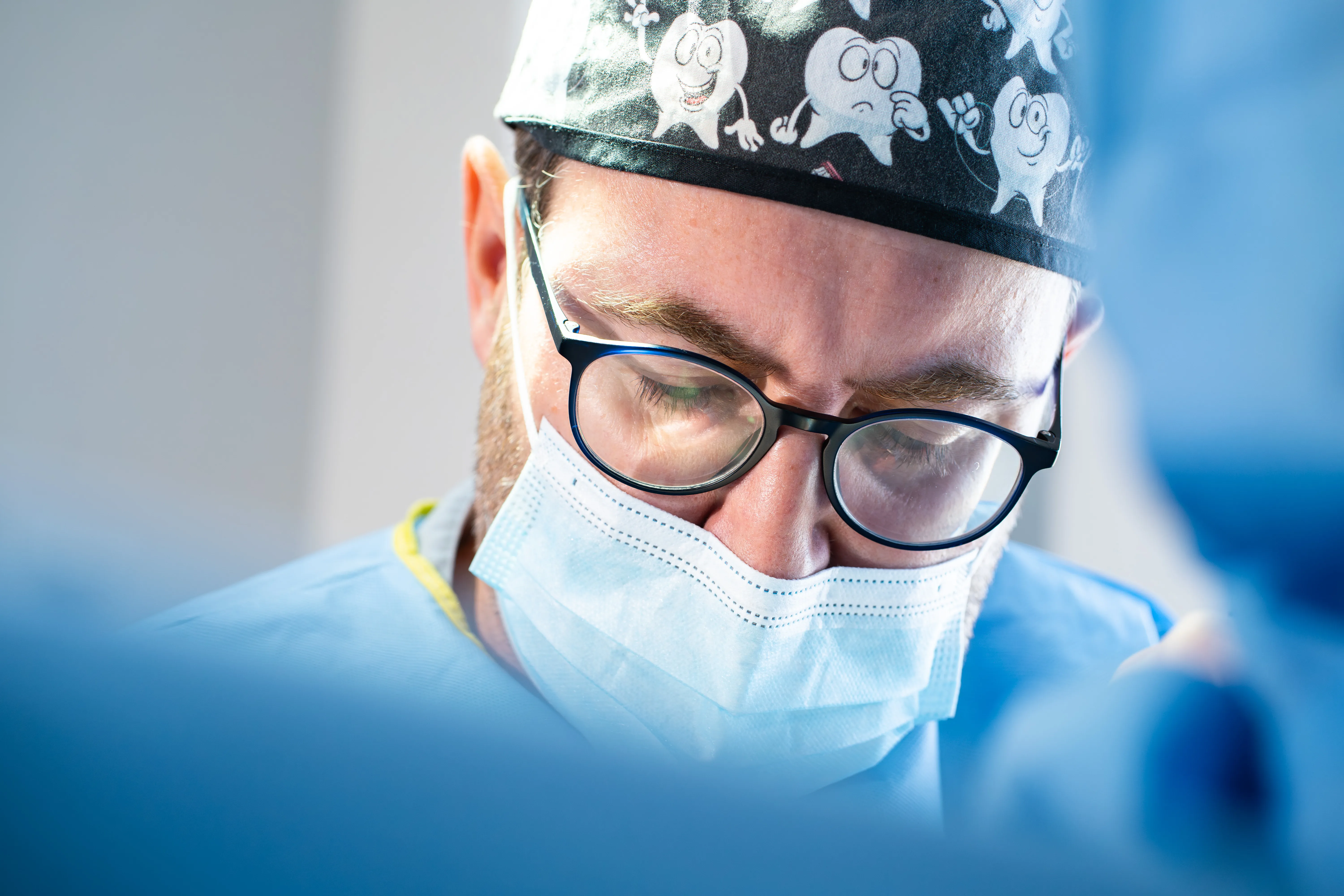 Praticien concentré pendant un soin, calot à motifs dents et masque chirurgical