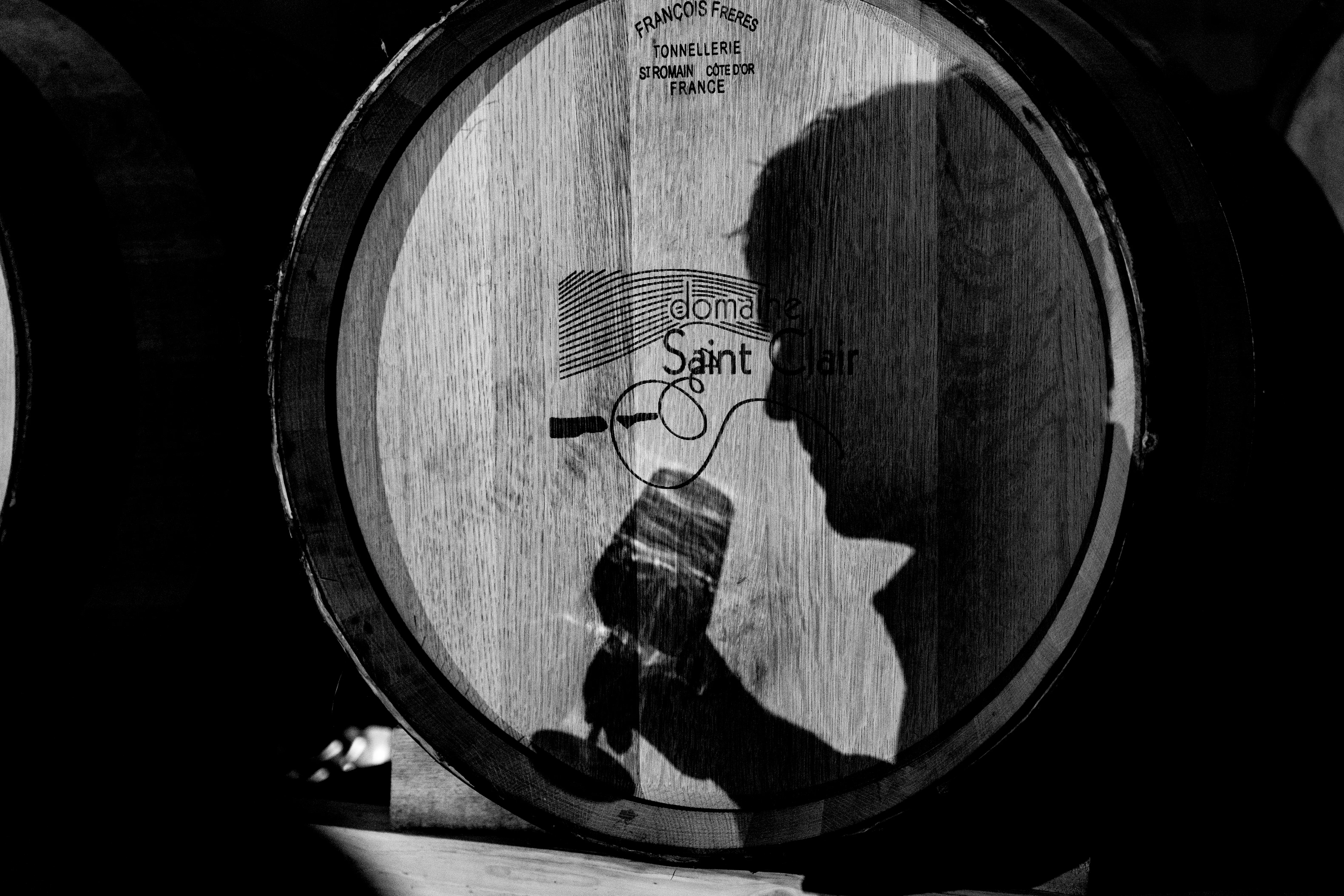 Ombre d'un verre porté au nez sur le fond de barrique marqué Domaine Saint Clair