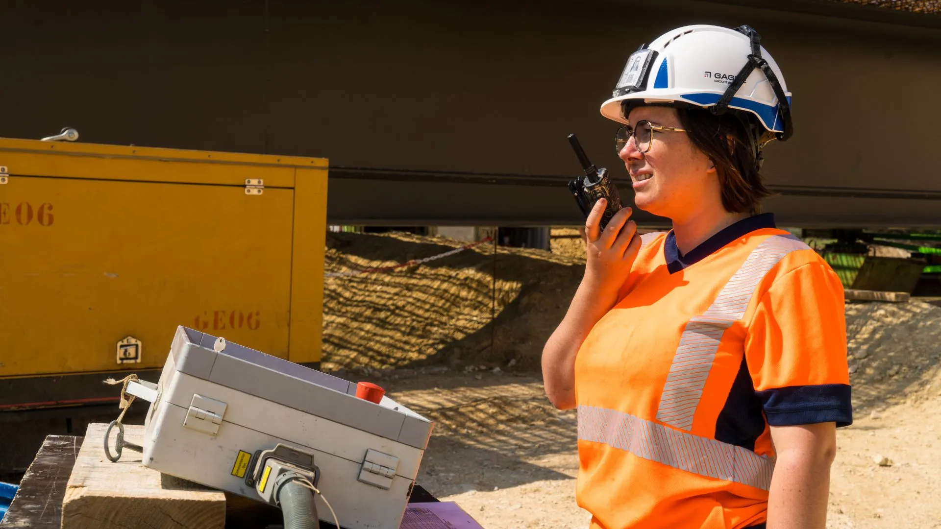 Conductrice de travaux au talkie-walkie sur le chantier, casque et gilet haute visibilité