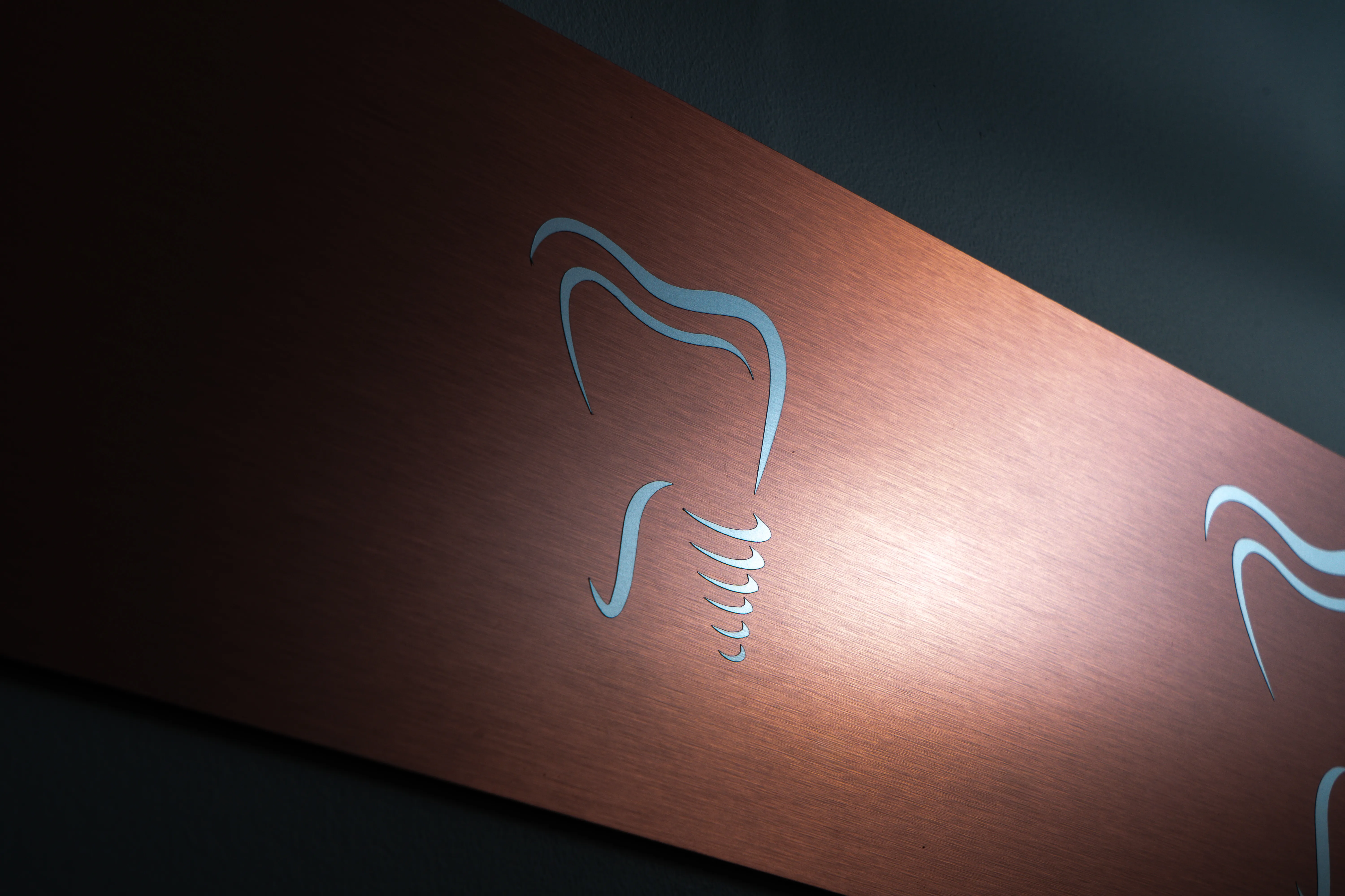 Logo dent implant du cabinet EVIDENT sur panneau métallique brossé