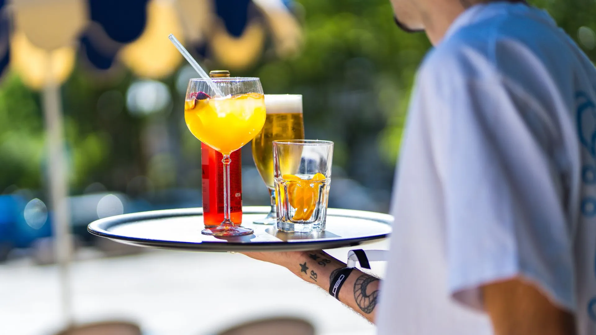 Serveur portant un plateau de cocktails et bières en terrasse