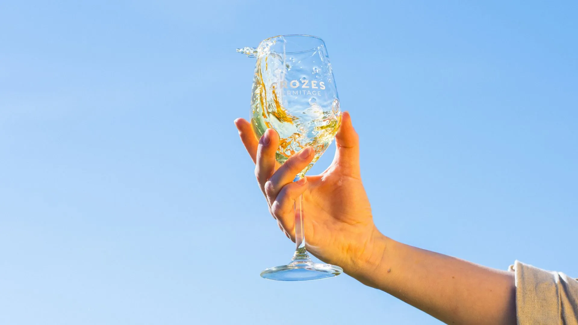 Main levant un verre gravé Crozes-Hermitage vers le ciel