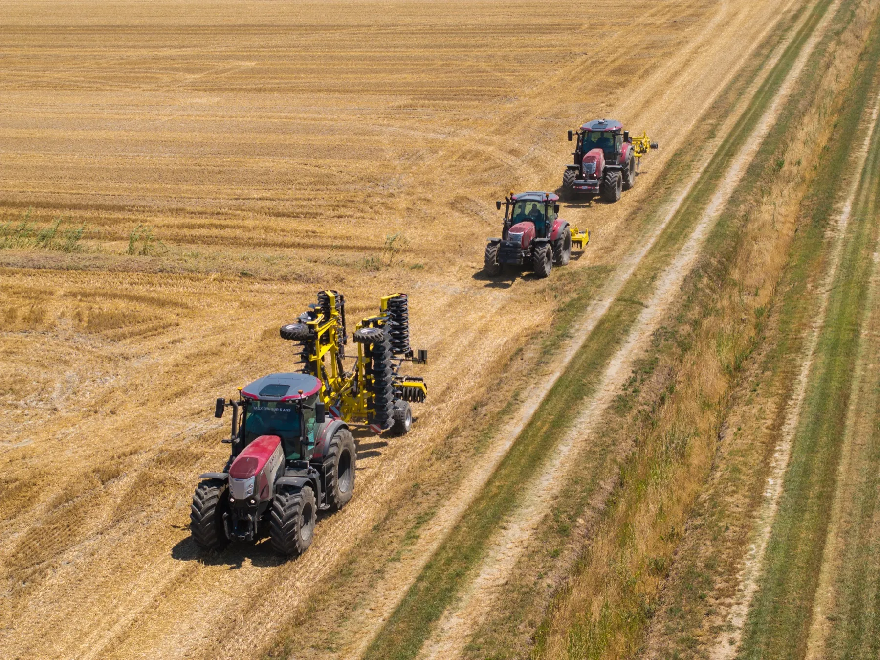 Trois tracteurs McCormick en démonstration dans un champ moissonné, vus du ciel