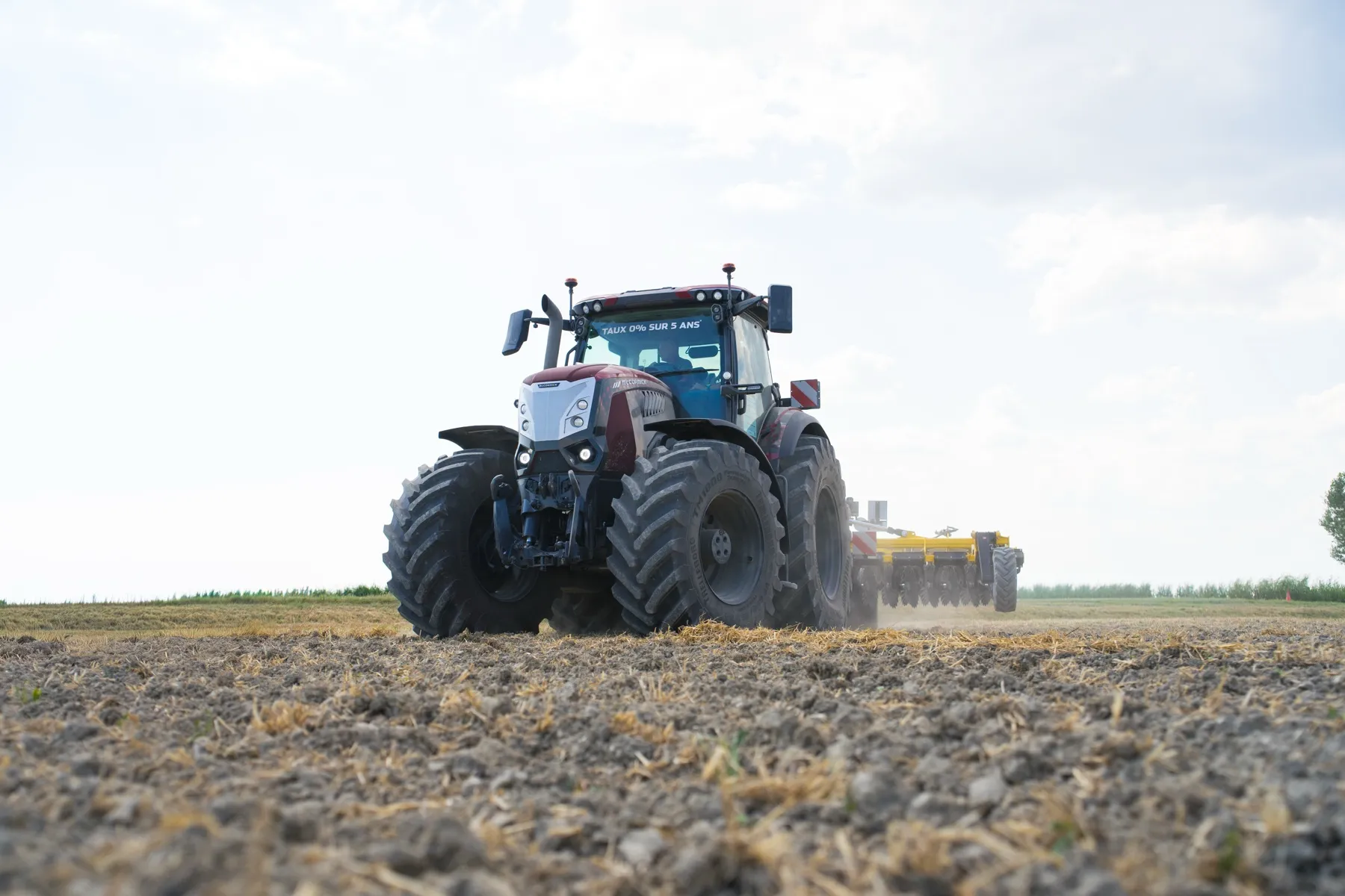 Tracteur McCormick au travail en contre-plongée, outil jaune attelé